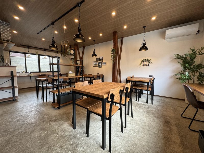 木のテーブルと黒い椅子、ペンダントライトが並ぶ店内